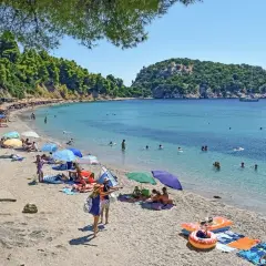 Słoneczny dzień na plaży w Chalkidiki. Ludzie opalają się, pływają w turkusowej wodzie, a kolorowe parasole rzucają cień.
