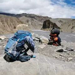Plecak czeka na dalszą drogę. W tle majestatyczne góry i rzeka, idealne miejsce na trekking w Himalajach.