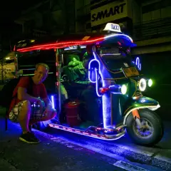 Uśmiechnięty turysta przy neonowym tuk tuk taxi w Tajlandii. Nocne światła tworzą magiczną atmosferę.